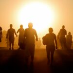silhouette of people standing on brown sand during sunset