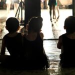Three children in black leotards sitting on a stage floor during a rehearsal